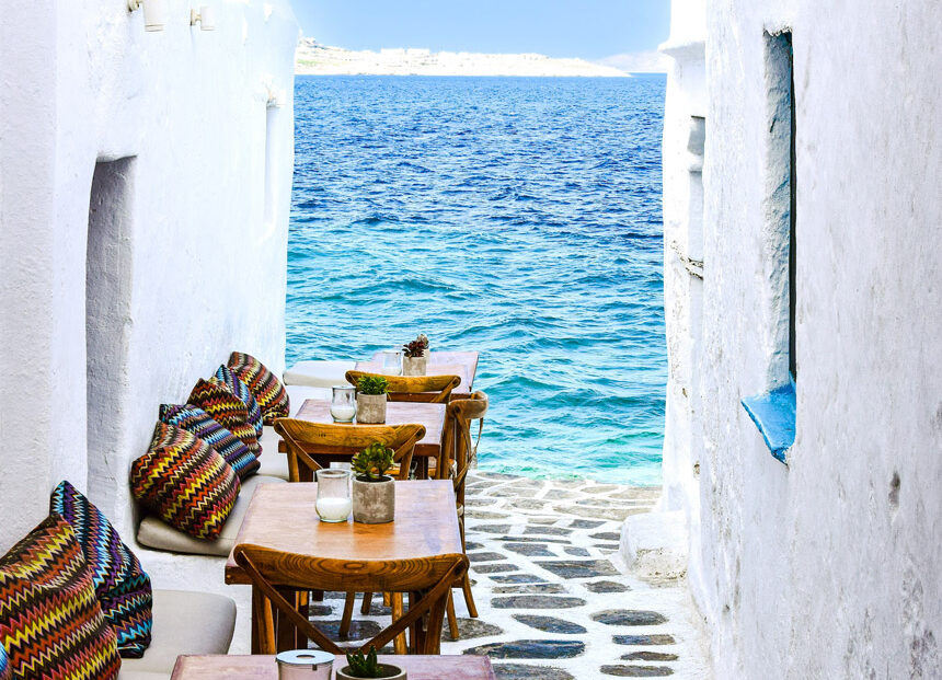 A seaview vista between two whitewashed houses with a cobbled stone alley between them, on a Greek island.